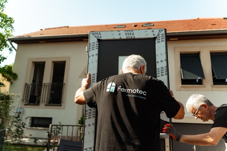 Deux menuisiers Otentik Fermotec apportant une porte d'entrée vers la maison