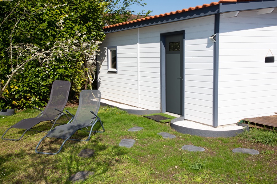 Porte de service grise donnant sur le jardin, sur une annexe en bardage blanc