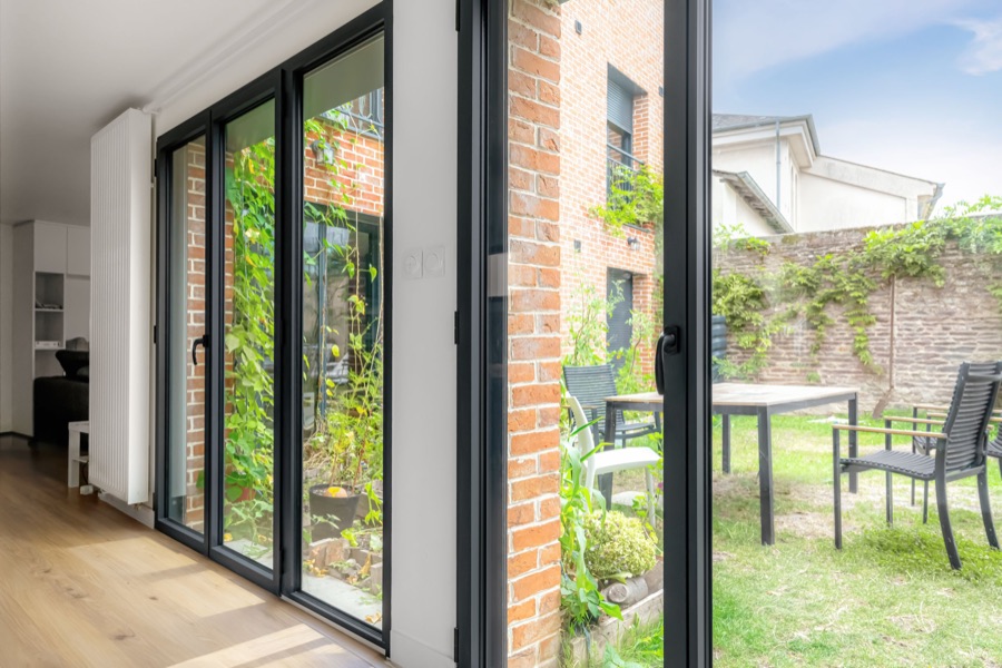 Portes-fenêtres aluminium noires ouvertes sur une cour et un jardin